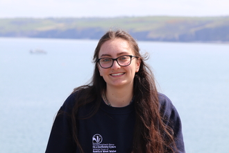 Maddy smiling at the camera, with the sea behind her